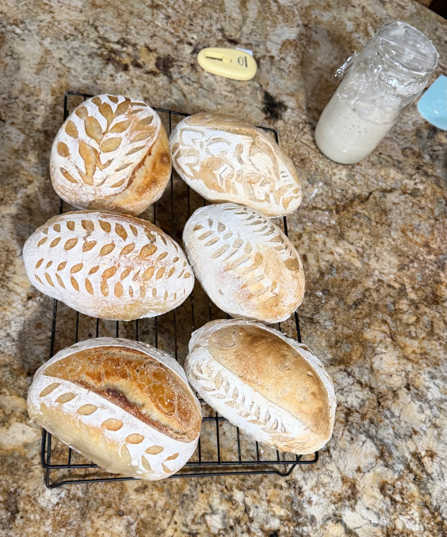 Six freshly baked loaves with intricate wheat and leaf scoring